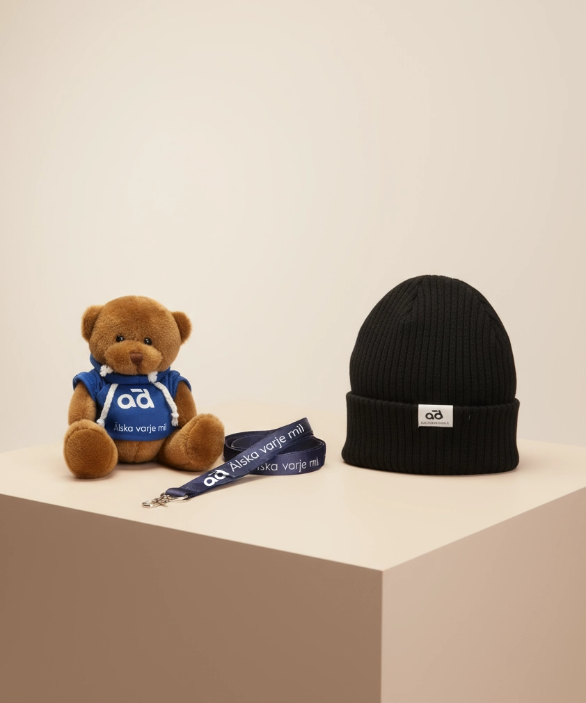 AD Bildelar merchandise, inklusive en brun nallebj&ouml;rn i en bl&aring; hoodie, en svart stickad m&ouml;ssa och en bl&aring; nyckelband d&auml;r det st&aring;r "&Auml;lska varje mil."